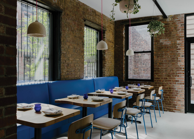 In the back dining room, where more original brick is exposed, custom tongue-and-groove tables with built-in silverware drawers front a long, blue banquette. Mycelium pendants with hot pink wiring hang above.