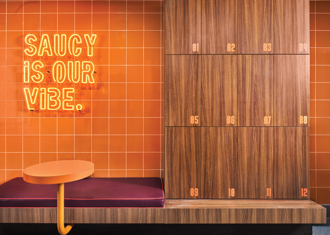 Saucy’s employee area is more than an afterthought, featuring upholstered bench seating along with design touches like orange wall tile and cubbies with mirrors
